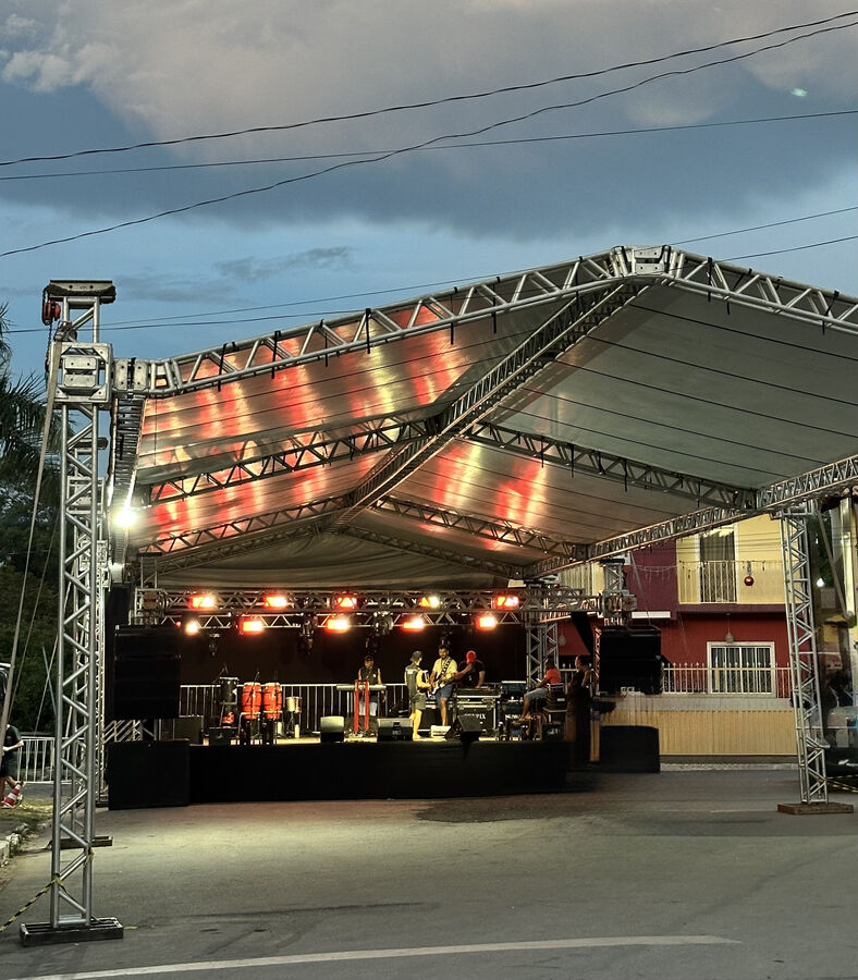 Palco com estrutura de treliça e iluminação, banda se apresentando ao entardecer