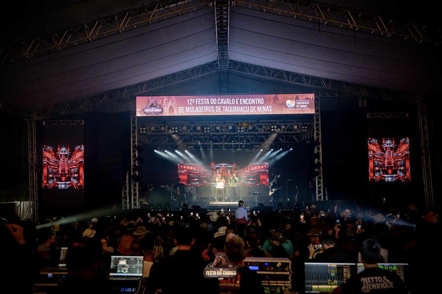 Palco montado com telões e iluminação cênica durante show noturno com público